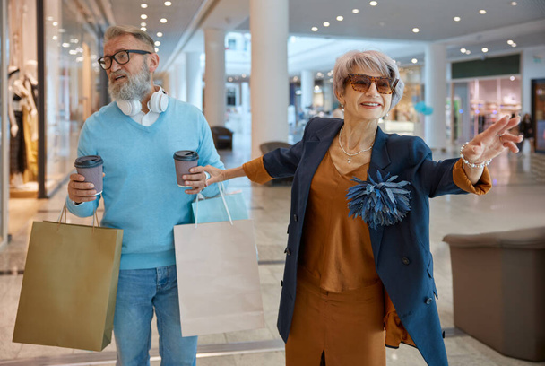 Oudere man en vrouw gaan winkelen op zwarte vrijdag weekends. Opgewonden oudere vrouw vraagt liefhebbende echtgenoot voor meer aankopen - Foto, afbeelding