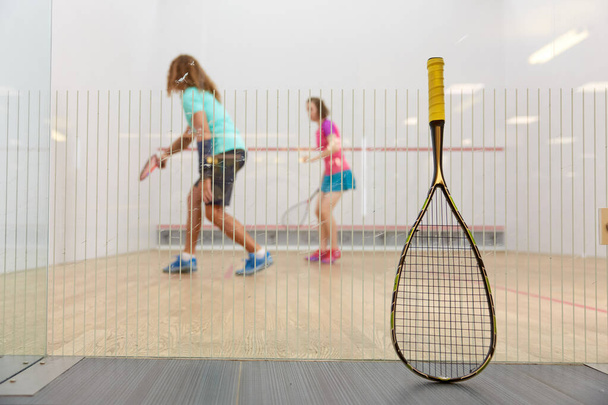Squash-Spielkonzept mit Schläger am Netz angelehnt und Sportlern, die gemeinsam auf verschwommenem Hintergrund spielen. Professionelle und qualitativ hochwertige Ausrüstung für das Schlägertraining - Foto, Bild