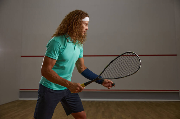 Konzentrierte junge erwachsene Squash-Spieler üben ihren Aufschlag, während sie das Spiel im Fitnessstudio üben. Sportlerporträt - Foto, Bild