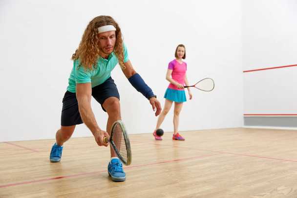 Jong sportief koppel dat squash beoefent op het sportveld. Focus op aantrekkelijke man slaan bal met racket - Foto, afbeelding