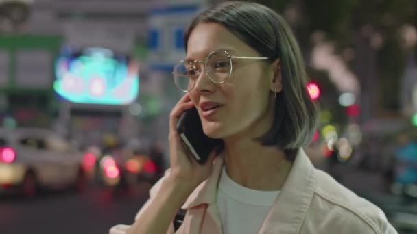 Hrudník se záběr mladé brunetky žena mluví na mobilním telefonu, zatímco stojí na ulici města v noci - Záběry, video