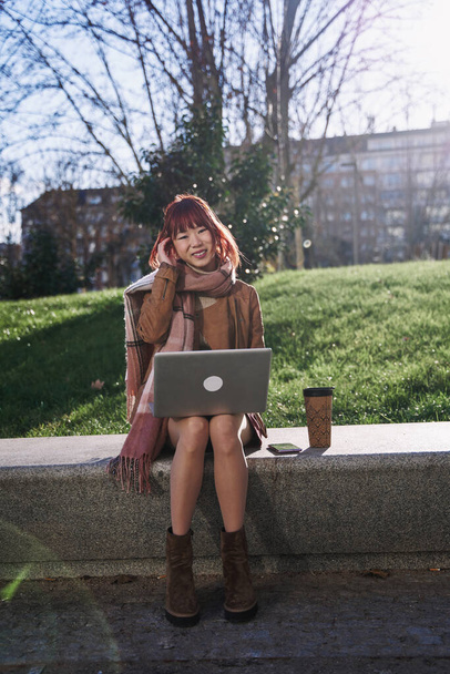 молодий китайський підліток використовує свій ноутбук у місті. жінка говорить на своєму мобільному телефоні. - Фото, зображення