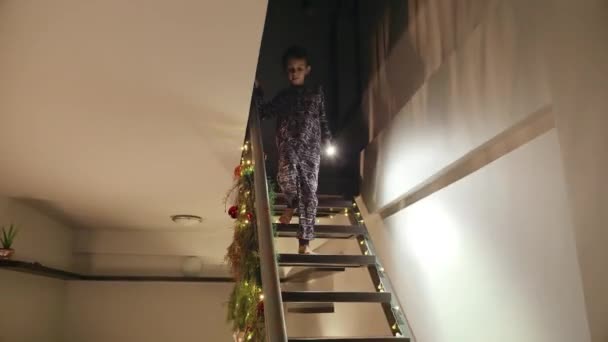 Kleine jongen in pyjama rent de trap af met fakkel op kerstavond. - Video