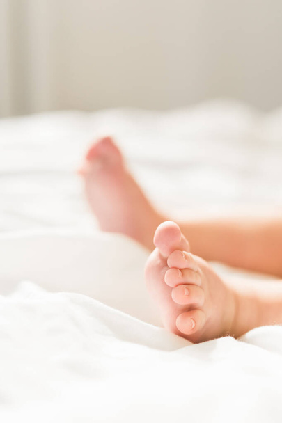 Ноги новорожденного в подгузнике, лежит на белой кровати, вид сверху. - Фото, изображение