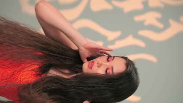 Verticaal portret van een jong model met lang zwart haar en heldere make-up. trage beweging, close-up, studio neergeschoten. - Video