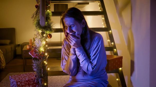 Noel ya da yeni yıl için süslenmiş, ağlayan genç bir kadının ahşap merdivenlerde oturmasını aydınlatan polis ya da ambulans ışıkları. Suç, ambulans, yaralanma, hukukla ilgili sorunlar ve kış tatillerinde hırsızlık ve kutlamalar - Fotoğraf, Görsel