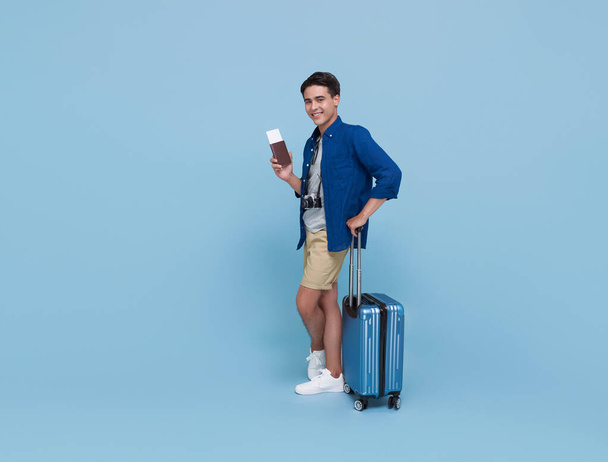 Feliz joven turista asiático portador de pasaporte con equipaje que va a viajar en vacaciones aislado sobre fondo azul. - Foto, imagen