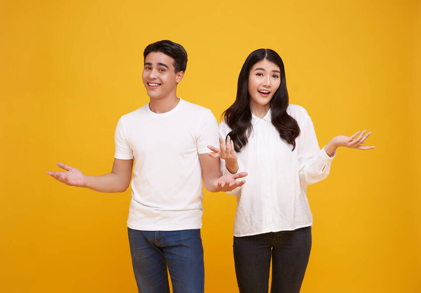 Portrait of happy cheerful awesome Asian couple with big smiles opening hands on isolated yellow background. - Foto, Bild