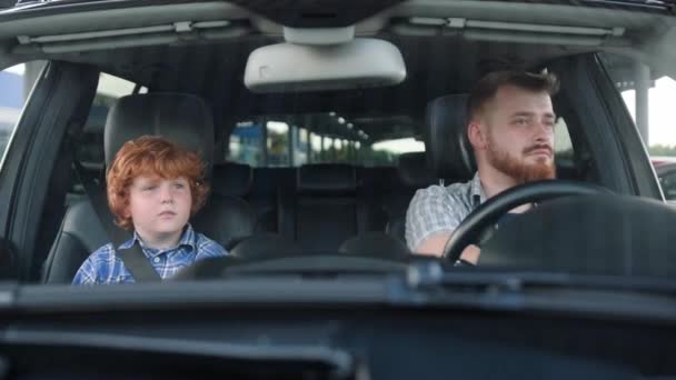Młody człowiek prowadzi samochód, podczas gdy mały chłopiec siedzi na miejscu pasażera. Transport, bezpieczeństwo, koncepcja rodziny. Zwolniony ruch - Materiał filmowy, wideo
