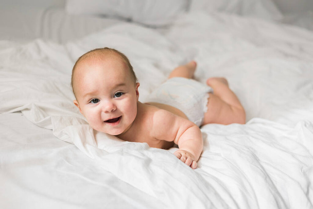 Uśmiechnięte noworodek na białym łóżku w domu, koncepcja szczęśliwego zdrowego niemowlęcia. Pokolenie alfa i gen alfa. - Zdjęcie, obraz