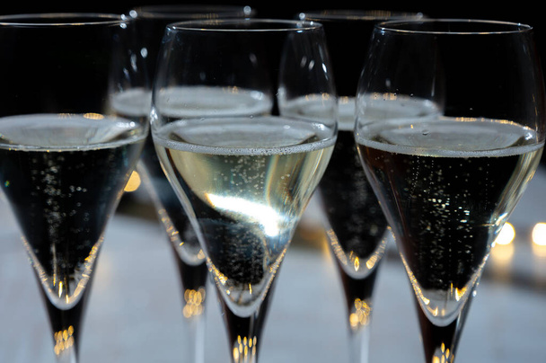 Πρωτοχρονιάτικο πάρτι, μικρές φυσαλίδες από brut σαμπάνια cava ή κρασί procecco σε ποτήρια τουλίπας με γιρλάντα φώτα σε σκούρο φόντο - Φωτογραφία, εικόνα