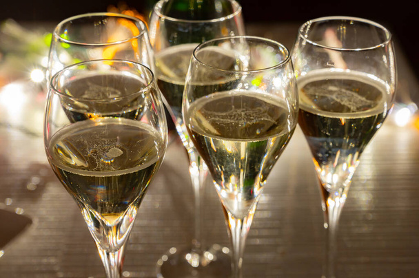 Przyjęcie noworoczne, małe bąbelki szampana cava lub wino prosecco w tulipanowych kieliszkach z lampkami girlandowymi na ciemnym tle - Zdjęcie, obraz