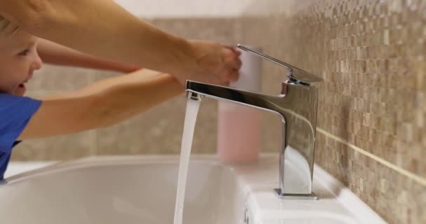 Anne ve küçük oğlu el yıkıyorlar. Anne, evdeki lavabonun üzerinde çocuklarının ellerini sabunla yıkamasına yardım ediyor. Sağlık ve hijyen kavramı. Yüksek kalite 4k görüntü - Video, Çekim