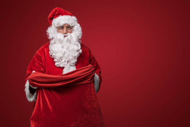 Άγιος Βασίλης σε κλασικό κόκκινο κοστούμι του, με αυτοπεποίθηση κρατώντας μια τσάντα - Φωτογραφία, εικόνα