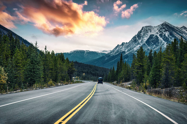 Kanada 'nın Alberta kentinde Banff Ulusal Parkı' ndaki kayalık dağlarda ve çam ormanlarında yol alan bir minibüsle manzaralı bir yolculuk. - Fotoğraf, Görsel