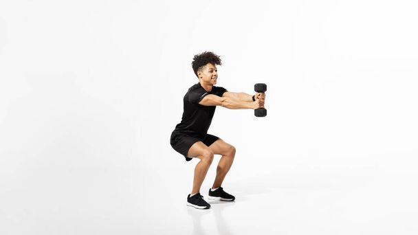 Νεαρός αθλητικός τύπος που κάθεται κρατώντας αλτήρες σε μυώδη χέρια κάνοντας προπόνηση σε λευκό φόντο στούντιο. Γυμναστική προπόνηση στο γυμναστήριο με έμφαση στη δύναμη και την ευεξία. Πανόραμα με ελεύθερο χώρο - Φωτογραφία, εικόνα