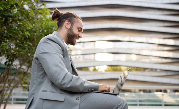 Biuro na zewnątrz. Happy Young Businessman Praca z laptopem na zewnątrz wobec nowoczesnego budynku miejskiego, Przystojny mężczyzna przedsiębiorca Odpowiadanie na maile, Millennial Man Korzystanie z pracy zdalnej, Kopiuj przestrzeń - Zdjęcie, obraz