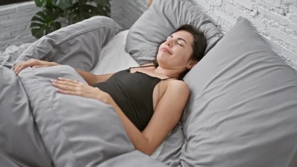 Ontspannen jonge Spaanse vrouw genieten van een gezellige en comfortabele rust, prachtig liggend in haar slaapkamer bed voor een ontspannen slaap thuis, kort haar draperen haar kussen in het ochtendlicht - Video