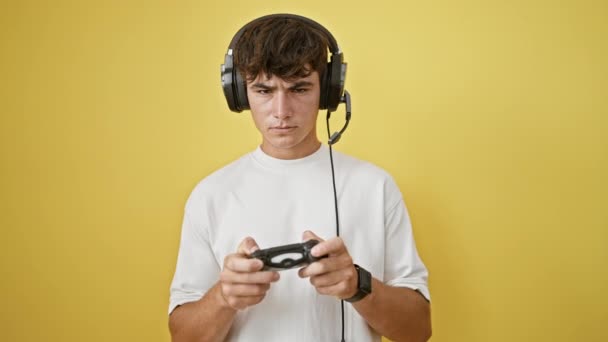 Verontrust jonge Spaanse tiener, verdiept in het spelen van een videospel, staat geïsoleerd tegen een gele achtergrond uiten woede, mogelijk verliezen - Video