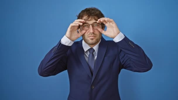 Sleepy young man in business suit fights fatigue, trying to force open tired eyes with fingers against isolated blue background - Footage, Video