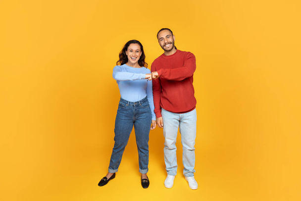 Couple Teamwork Concept. Portrait Of Smiling Guy And Lady Bumping Fists, Looking At Camera, Celebrating Success Partnership Triumph Standing Isolated Over Yellow Studio Background, Full Length - Photo, Image