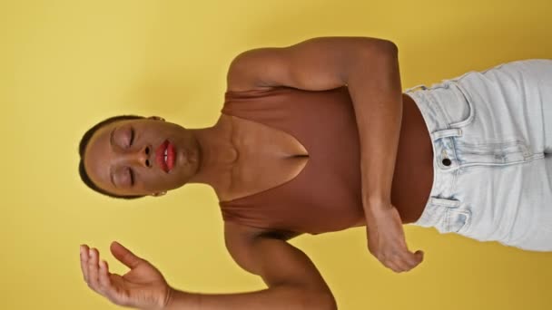 Przygnębiona Afroamerykanka, znudzona i zmęczona, stoi myśląc o swoich problemach, ramionach skrzyżowanych na żółtym tle - Materiał filmowy, wideo