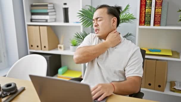 Στρεσαρισμένος νεαρός Κινέζος επιχειρηματίας που παλεύει με τον αυχενικό πόνο, κολλημένος σε φορητό υπολογιστή στο γραφείο - Πλάνα, βίντεο