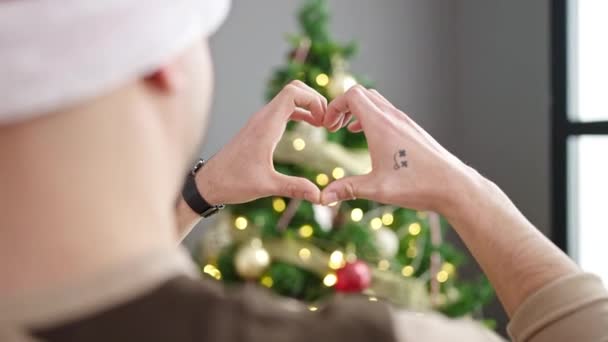 Hombre árabe joven haciendo gesto de corazón de pie junto al árbol de Navidad en casa - Imágenes, Vídeo