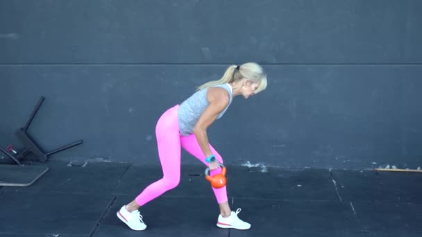 Full body real time van fit sportvrouw in sportkleding met blonde paardenstaart doet een arm rij oefening met zware kettlebell tijdens de training in de sportschool - Video