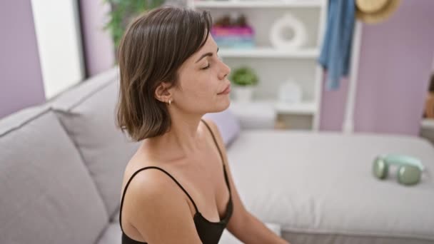 Nuori kaunis latino nainen istuu sohvalla hengitys suljetuin silmin kotona - Materiaali, video