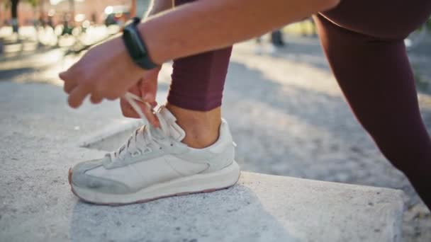 Frau bindet Schnürsenkel an sportliche Turnschuhe in Nahaufnahme. Unbekannte Sportlerin bereitet sich in Sommerstadt auf das Lauftraining vor. Unerkennbarer Läufer schnürt Schuhe für Marathon im Stadion - Filmmaterial, Video