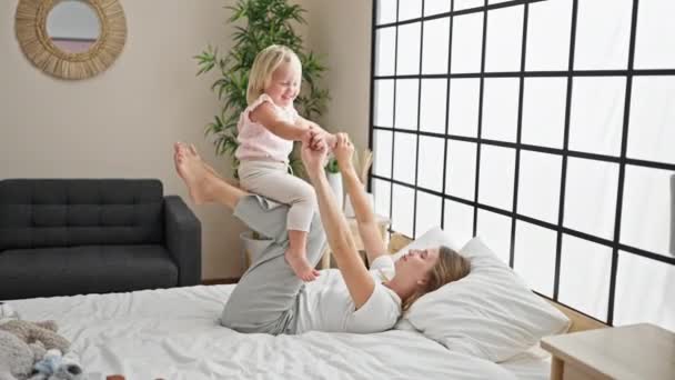 Blanke moeder en dochter gelukkig spelen in bed, tillen het vrolijke kind hoog in de lucht, genieten van een ontspannen ochtend samen in hun gezellige slaapkamer thuis. - Video