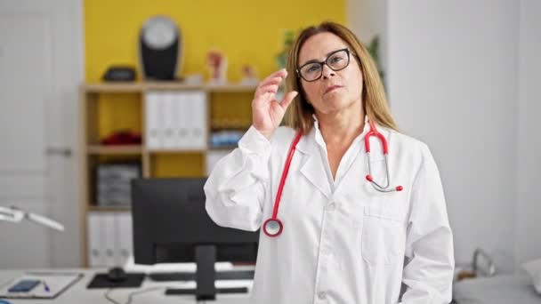 Keski-ikä latino nainen lääkäri seisoo vakava ilme klinikalla - Materiaali, video