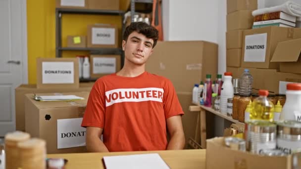 Mladý hispánský teenager ukazuje na dobrovolnickou uniformu usmívající se v charitativním centru - Záběry, video