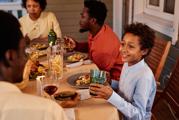 Porträt eines lächelnden afroamerikanischen Jungen beim Abendessen mit der Familie auf der Terrasse im Freien - Foto, Bild