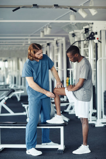 Junger Arzt in Uniform untersucht Patient vor Sporttraining im Fitnessstudio - Foto, Bild