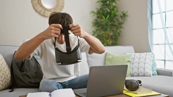 Όμορφος νεαρός Ισπανός έφηβος απορροφημένος στον κυβερνοχώρο, χαλαρώνοντας στον καναπέ με ένα φορητό υπολογιστή, γυαλιά VR, μελετώντας στο σαλόνι στο σπίτι. - Πλάνα, βίντεο