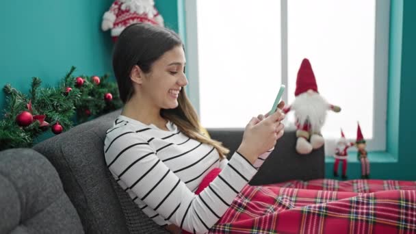 Молода красива іспаномовна жінка використовує смартфон, що святкує Різдво вдома - Кадри, відео