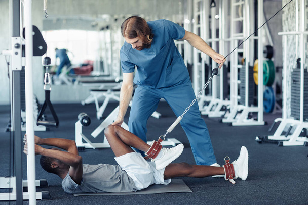 Врач в форме, работающий с физическим состоянием пациента, использует спортивный инвентарь, чтобы размять ноги - Фото, изображение