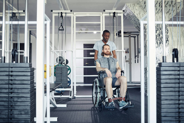 Travailleur médical poussant le fauteuil roulant avec le patient le long du club de santé, ils vont pour des exercices sportifs - Photo, image