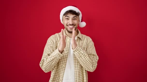 Hombre árabe joven con sombrero de Navidad con expresión alegre sobre fondo rojo aislado - Metraje, vídeo