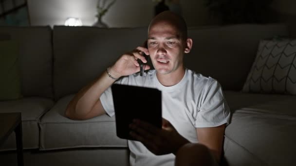 Nuori latino mies käyttää kosketuslevy puhuu älypuhelimeen istuu lattialla kotona - Materiaali, video