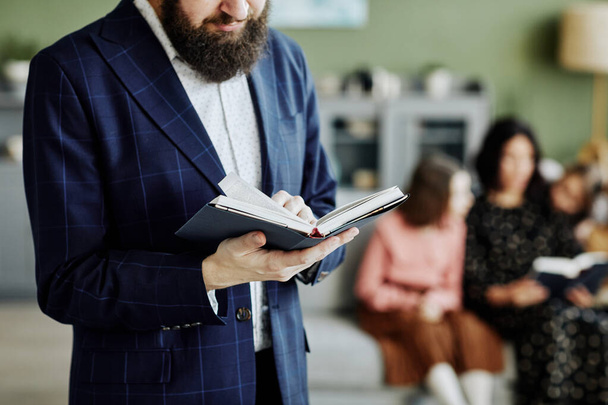 Обрізаний знімок бородатого єврейського чоловіка, який читає книгу вдома з сім'єю на задньому плані, копіювання простору - Фото, зображення