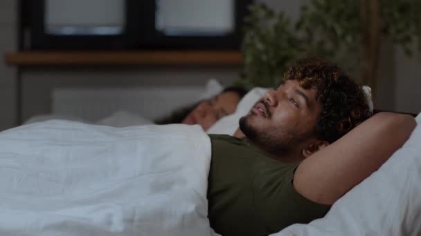 Trastorno del sueño. Retrato de cerca del joven árabe que sufre de insomnio, respirando duro, acostado en la cama con su esposa dormida por la noche, rastreando disparos - Metraje, vídeo