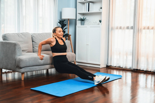 健康的なフィットボディライフスタイルのコンセプトとしてホームエクササイズをプッシュして効果的なターゲティング筋肉のための家具を使用して運動とアクティブなシニア女性. クロート - 写真・画像