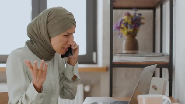 Problemas de negocios. Primer plano retrato de irritada mujer de Oriente Medio ceo hablando en el teléfono celular con el empleado, regañando sobre los errores de contrato en el ordenador portátil, la comprobación de papeles en línea, seguimiento de disparo - Metraje, vídeo
