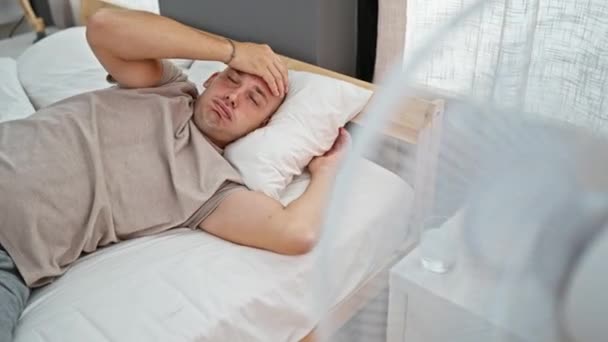 Nuori latino mies makaa sängyllä hikoilu käyttäen tuuletin makuuhuoneessa - Materiaali, video