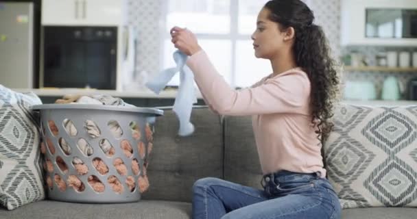 .Woman, basket and folding laundry on sofa with baby clothes, cleaning and thinking in home for hygiene. Young mom, fabric and housework with care, cotton or material on couch with plastic container - Footage, Video