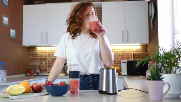 Γυναίκα δοκιμάζει smoothie κατασκευασμένο από φρούτα στο μπλέντερ στην κουζίνα του σπιτιού. έννοια και ιδέα της υγιεινής διατροφής, χορτοφαγία και συνειδητή διατροφή - Πλάνα, βίντεο