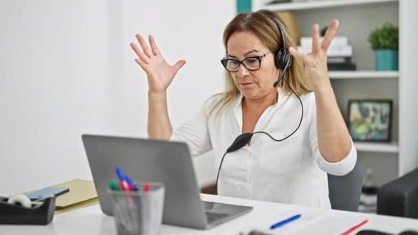 Középkorú spanyol üzleti dolgozó laptoppal és fejhallgatóval stresszes az irodában - Felvétel, videó